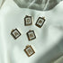 Five square initial letter pendants featuring sparkling rhinestone letters rest on a white silk backdrop.