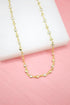 A delicate gold chain necklace with alternating heart charms and sparkling CZ crystals rests on a white display against a pink background.