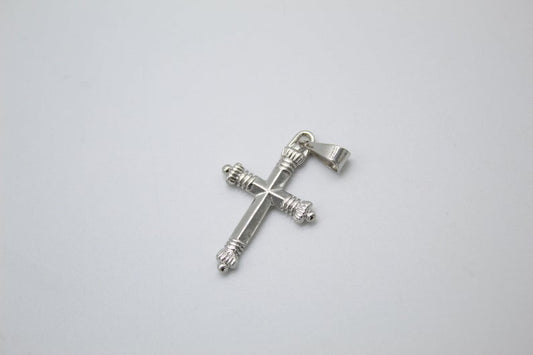 A polished silver cross pendant featuring decorative fluted ends rests centrally on a clean white surface.