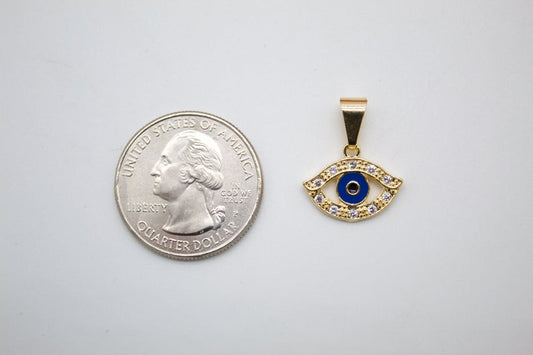 A gold evil eye pendant with blue enamel and cubic zirconia stones rests next to a US quarter coin for scale.