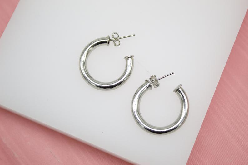 A pair of thick silver hoop earrings rests on a white display block.