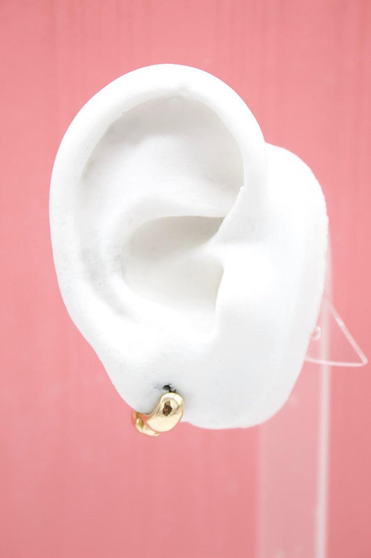A white mannequin ear displays a small gold hoop earring against a pink background.