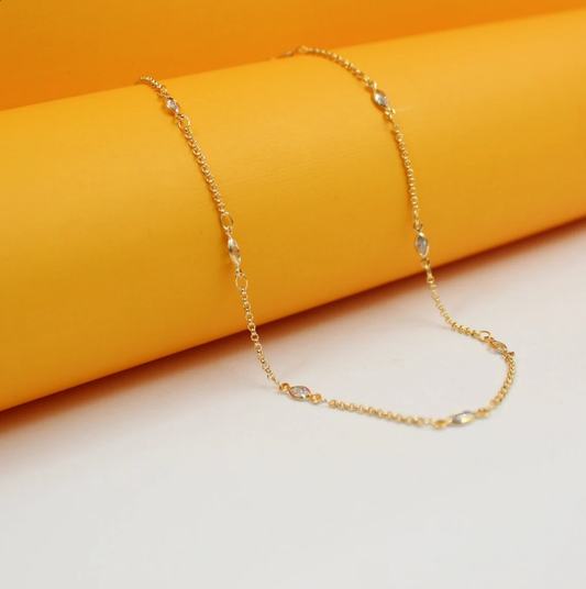 A delicate gold chain necklace with interspersed crystal stones drapes across a vibrant orange and white display.