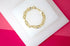 A shiny gold mariner link bracelet rests on a white display block against a vibrant pink background.