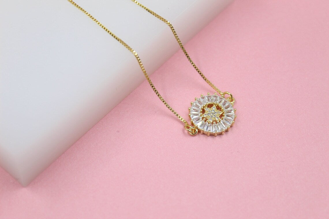 A delicate gold necklace with a round, crystal-embellished pendant rests on a pink and white surface.