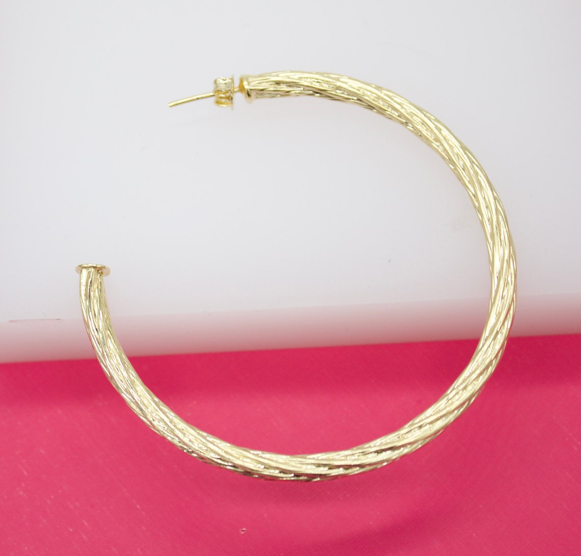 A large, textured gold hoop earring rests against a white and pink background.