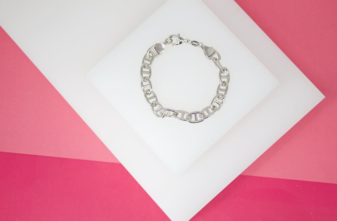 A sleek silver link bracelet rests gracefully on a white geometric platform against a vibrant pink background.