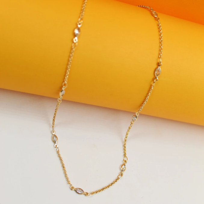A delicate gold chain necklace featuring sparkling marquise-cut zircon stones rests against a vibrant yellow and white background.