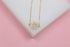 A delicate gold chain necklace with a circular pendant featuring sparkling baguette and round cubic zirconia stones rests on a white display against a pink background.