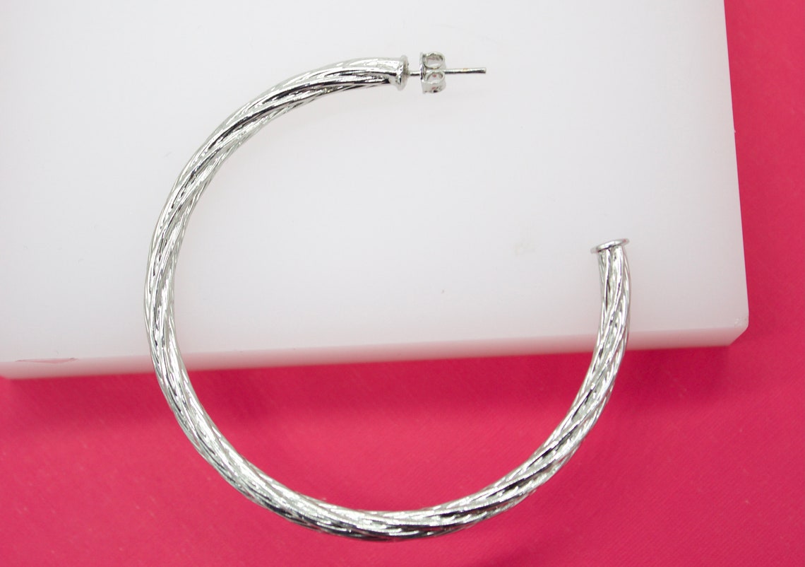 A large textured silver hoop earring rests on a white display against a vibrant pink background.