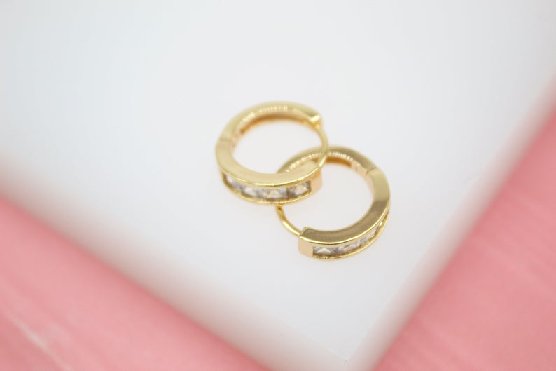 A pair of gold hoop earrings inlaid with sparkling cubic zirconia crystals rests on a white display surface.