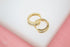 A pair of gold hoop earrings inlaid with sparkling cubic zirconia crystals rests on a white display surface.