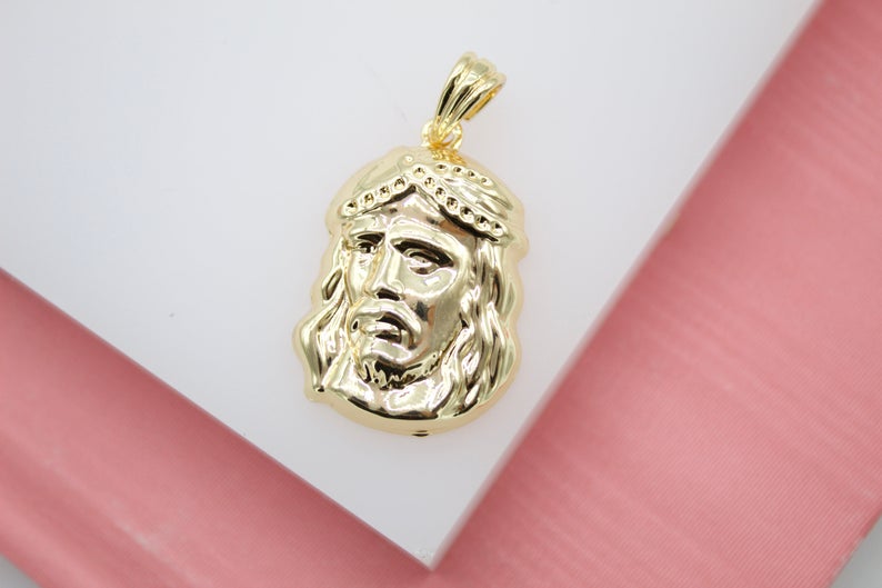 A polished gold Jesus face pendant rests on a white display surface.