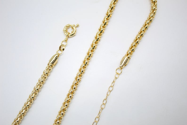 A shiny gold chain necklace lies displayed against a clean white background, showcasing its detailed textured links and clasp.