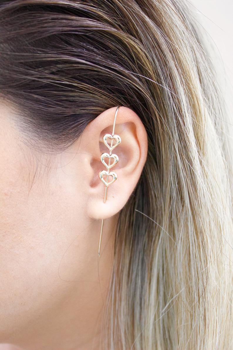 A woman wears a delicate gold heart ear crawler hugging the contour of her ear.