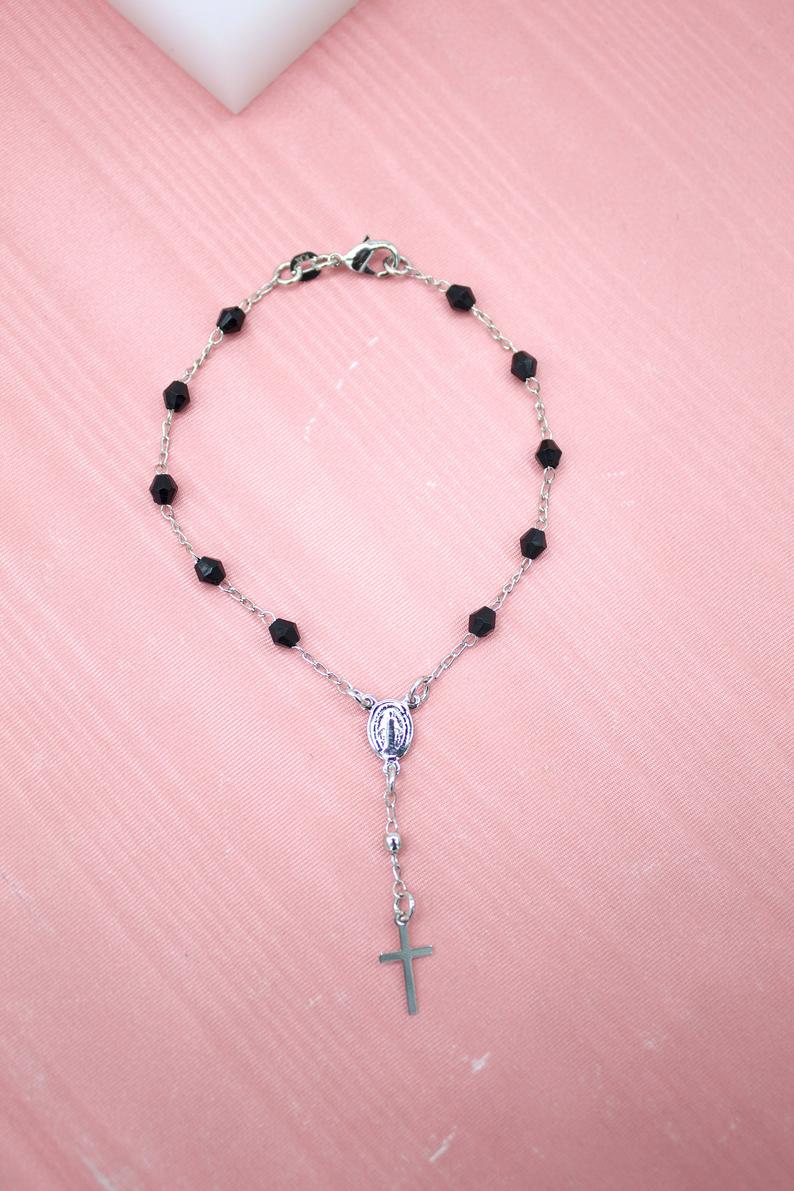 A dainty silver rosary bracelet featuring faceted black beads rests on a soft pink surface.