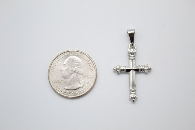 A silver cross pendant lies next to a US quarter coin on a light surface, showing its scale.