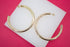 Large thick gold hoop earrings rest on a white display against a vibrant pink background.