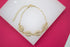 A delicate gold-plated cowrie shell bracelet featuring shimmering pave crystals rests on a white display against a vibrant pink background.