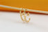 A pair of gold spike hoop earrings hangs delicately from a wooden stick against a soft-focus background.