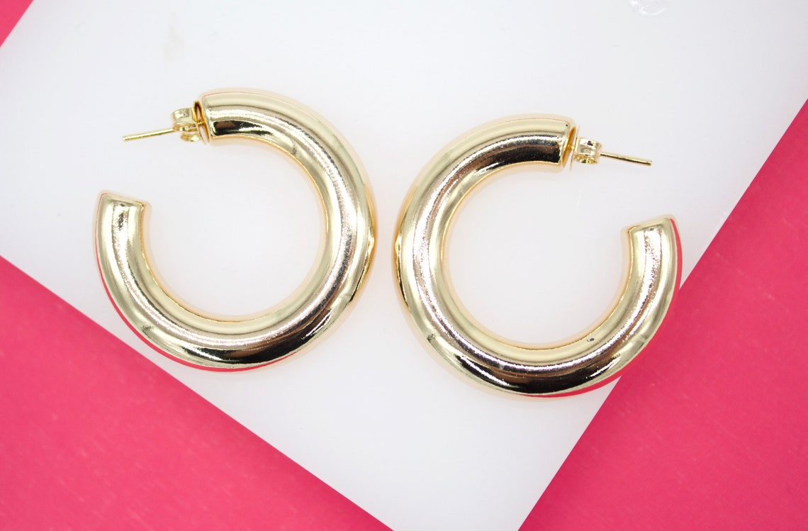 A pair of shiny gold hoop earrings rests on a white and pink background.