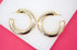 A pair of shiny gold hoop earrings rests on a white and pink background.