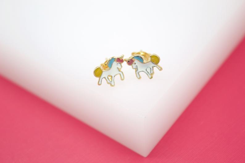 A pair of charming gold unicorn stud earrings rests against a white and pink display surface.