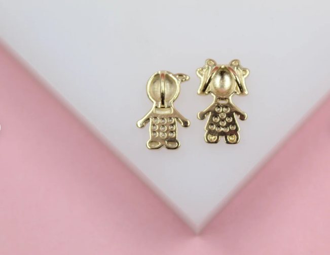 A pair of gold earrings shaped like a boy and a girl rest on a white and pink surface.