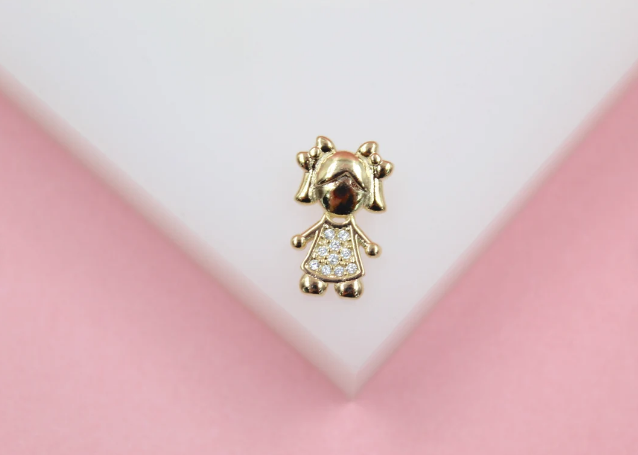 A gold pendant shaped like a little girl wearing a dress encrusted with sparkling cubic zirconia stones rests on a white display surface.