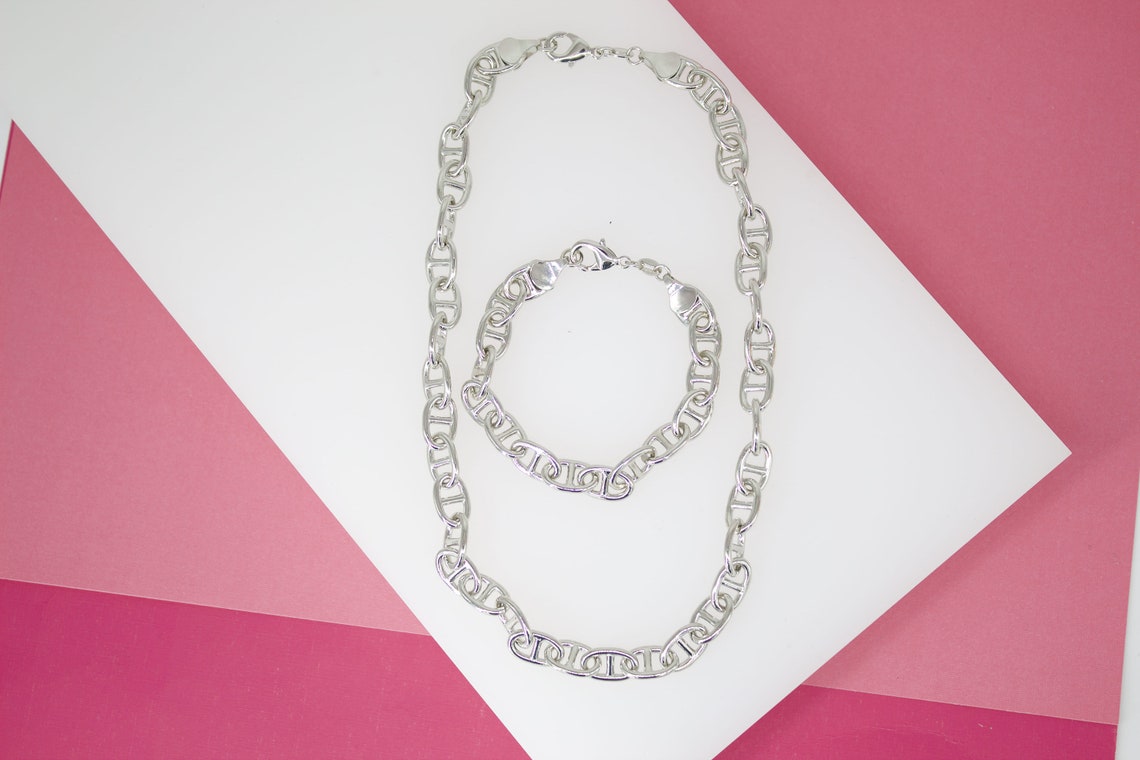 A matching silver Mariner chain necklace and bracelet rest on a white and pink geometric background.