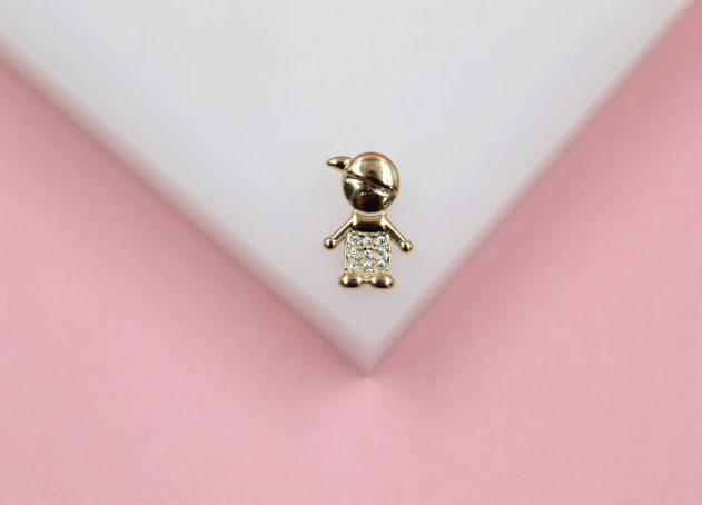 A gold pendant shaped like a boy wearing a cap and sparkling crystal shirt rests on a white display surface.