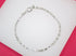 A delicate silver box chain bracelet rests on a white display surface against a vibrant pink background.