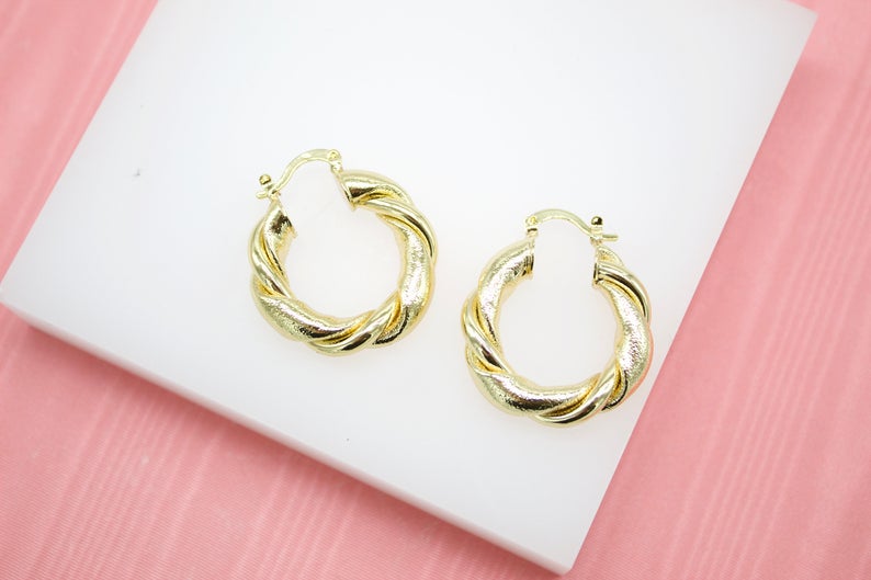 A pair of textured gold hoop earrings rests neatly on a white surface.