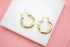 A pair of textured gold hoop earrings rests neatly on a white surface.