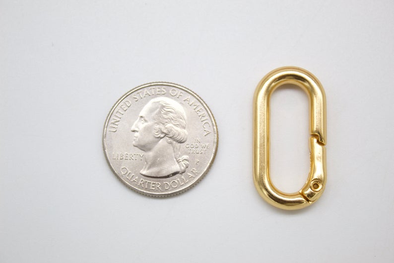 A gold oval spring gate ring lies next to a US quarter for size comparison.