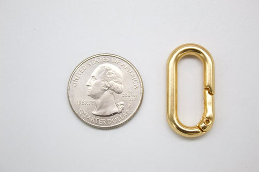 A gold oval spring gate ring lies next to a US quarter for size comparison.