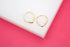 A pair of small gold hoop earrings with a subtle heart shape rests on a white block against a bright pink background.