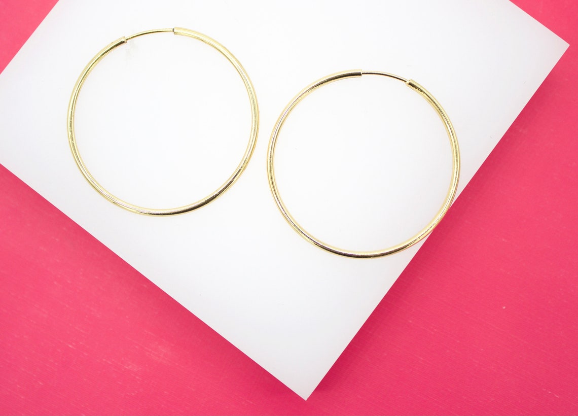 A pair of classic gold hoop earrings rests neatly on a white display surface against a vibrant pink background.