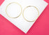 A pair of classic gold hoop earrings rests neatly on a white display surface against a vibrant pink background.