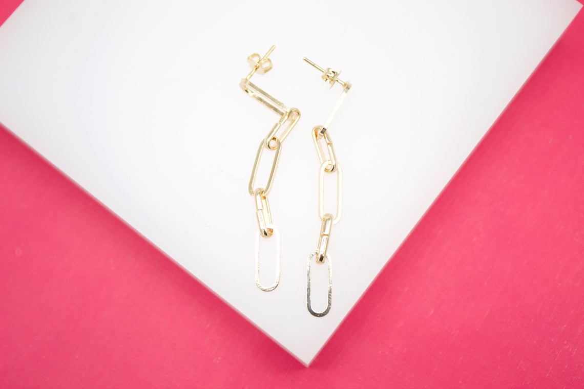 A pair of elegant gold chain link dangle earrings rests on a white and bright pink background.