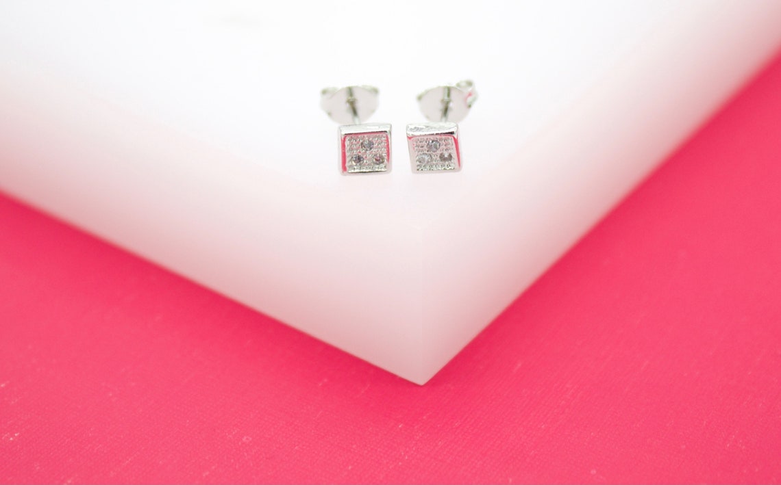 A pair of silver square stud earrings featuring tiny crystal accents rests neatly on a white surface.