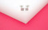 A pair of silver square stud earrings featuring tiny crystal accents rests neatly on a white surface.