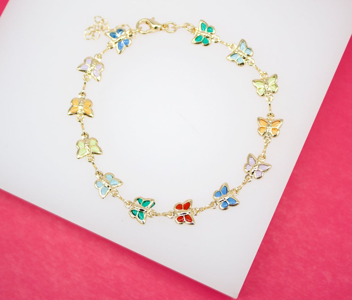 A gold butterfly chain bracelet features colorful enamel charms arranged in a circle on a white and pink background.