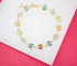 A gold butterfly chain bracelet features colorful enamel charms arranged in a circle on a white and pink background.