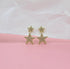 Sparkling gold star stud earrings rest against a soft pink and white textured backdrop.