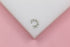 A detailed silver ear cuff features sparkling cubic zirconia stones, small spikes, and delicate pearls, resting on a white display against a soft pink background.