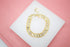 A gold-plated link bracelet rests on a white display surface against a pink background.