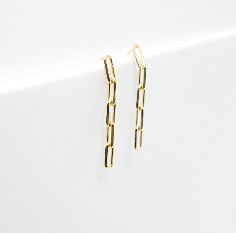 A pair of delicate gold paperclip chain drop earrings rests elegantly against a clean white background.