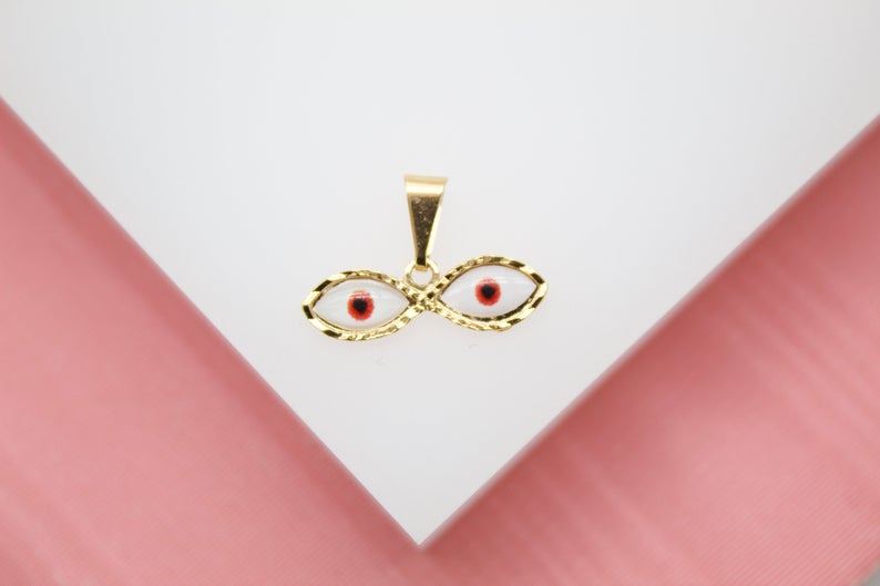 A gold evil eye pendant features white enamel and a central red and black pupil design against a white and pink background.