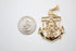 A gold anchor pendant featuring Our Lady of Guadalupe rests beside a US quarter coin to show its scale.